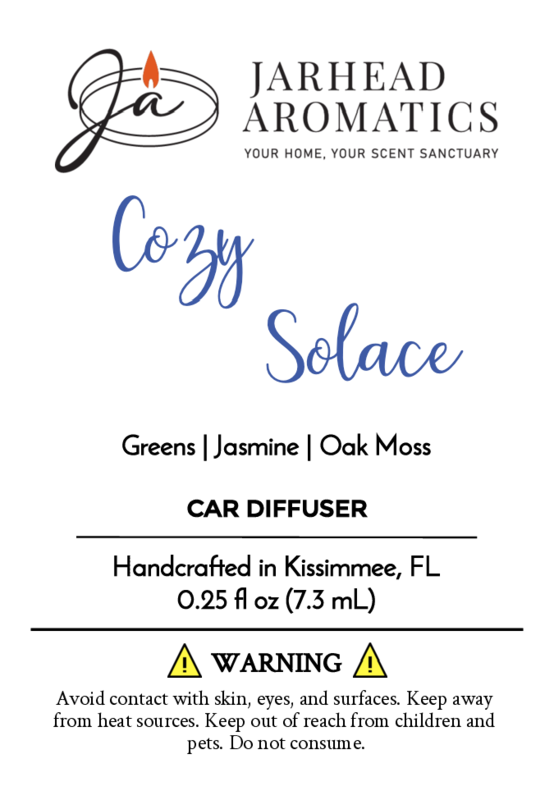 A product label for Jarhead Aromatics Cozy Solace - Car Diffuser from the Fall Collection, highlighting a jasmine scent with fresh greens and oak moss. Warning symbols and caution text appear at the bottom.