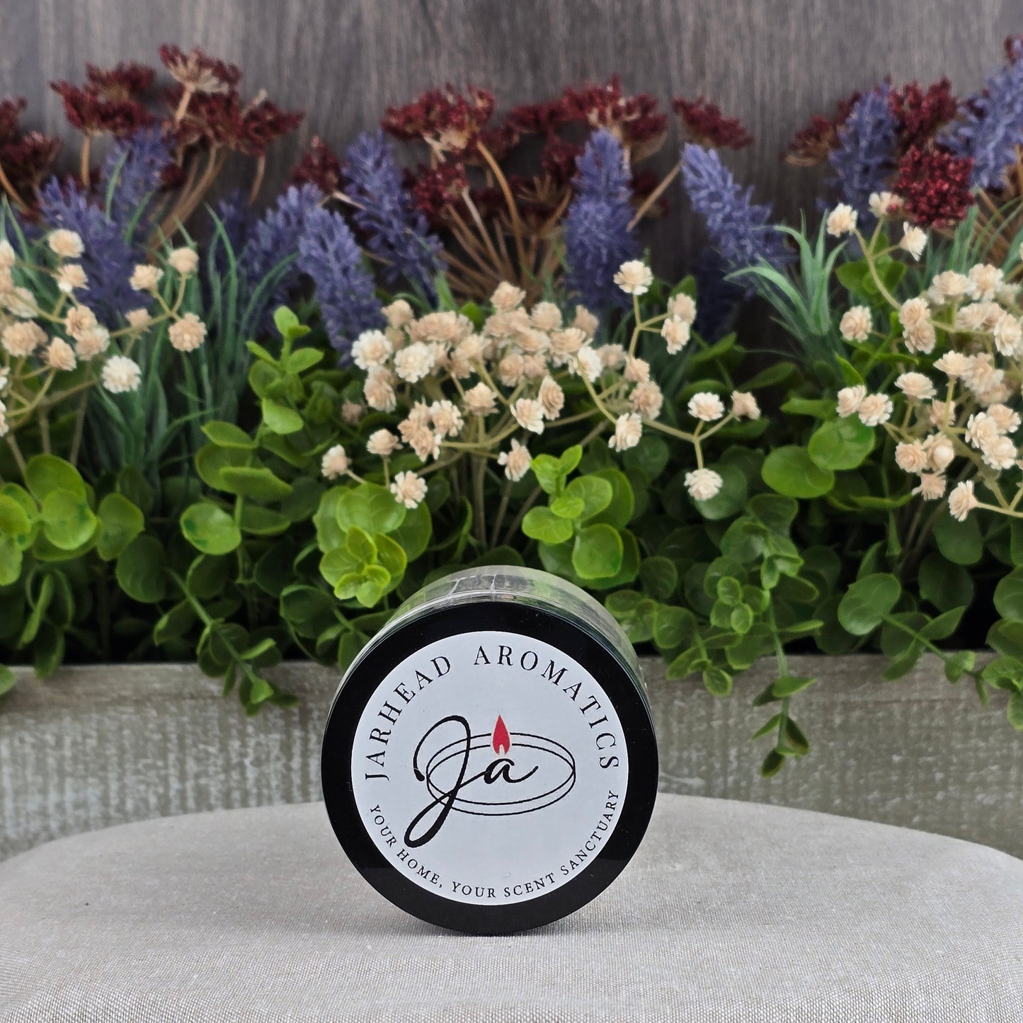 A Jarhead Aromatics Unscented Oats Milk Bath sits on a light surface in front of a planter with artificial green leaves, purple lavender, and white dried flowersโperfect for sensitive skin with its all-natural goat milk and buttermilk formula.