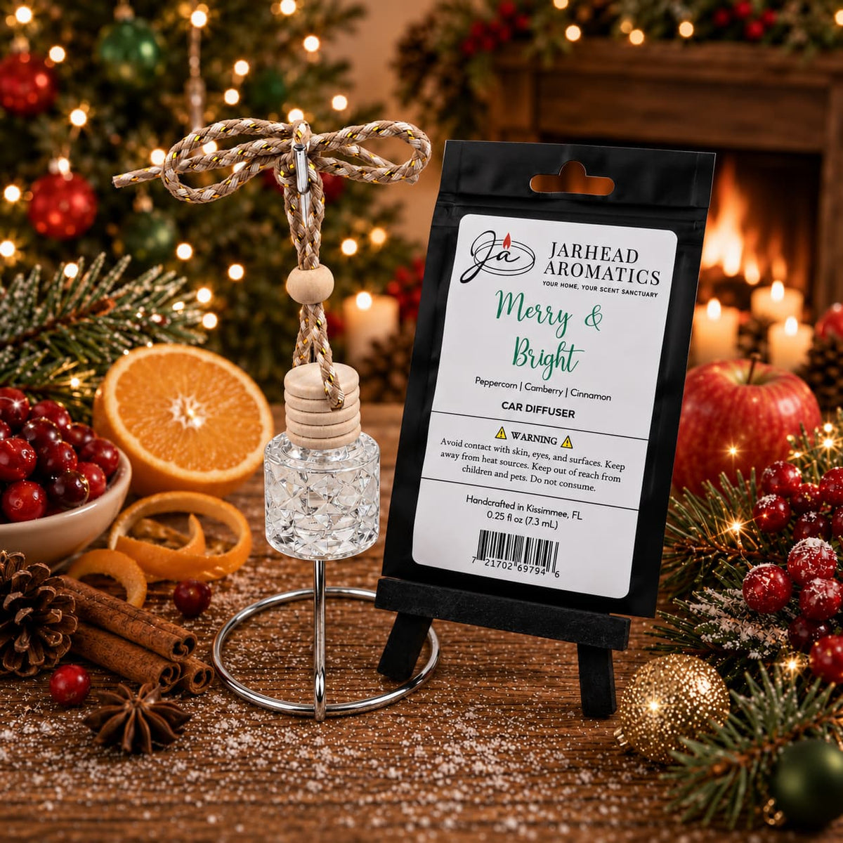 A Jarhead Aromatics Merry & Bright Car Diffuser with a wooden bead and hanging cord stands next to its black product label on a miniature easel, set against a festive background with a fireplace and holiday tree.
