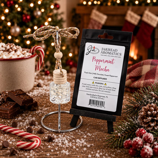 A Jarhead Aromatics Peppermint Mocha Car Diffuser | Chocolate Mint hanging in a geometric glass bottle, displayed next to its packaging on a table set with chocolate, candy canes, and festive holiday decor.