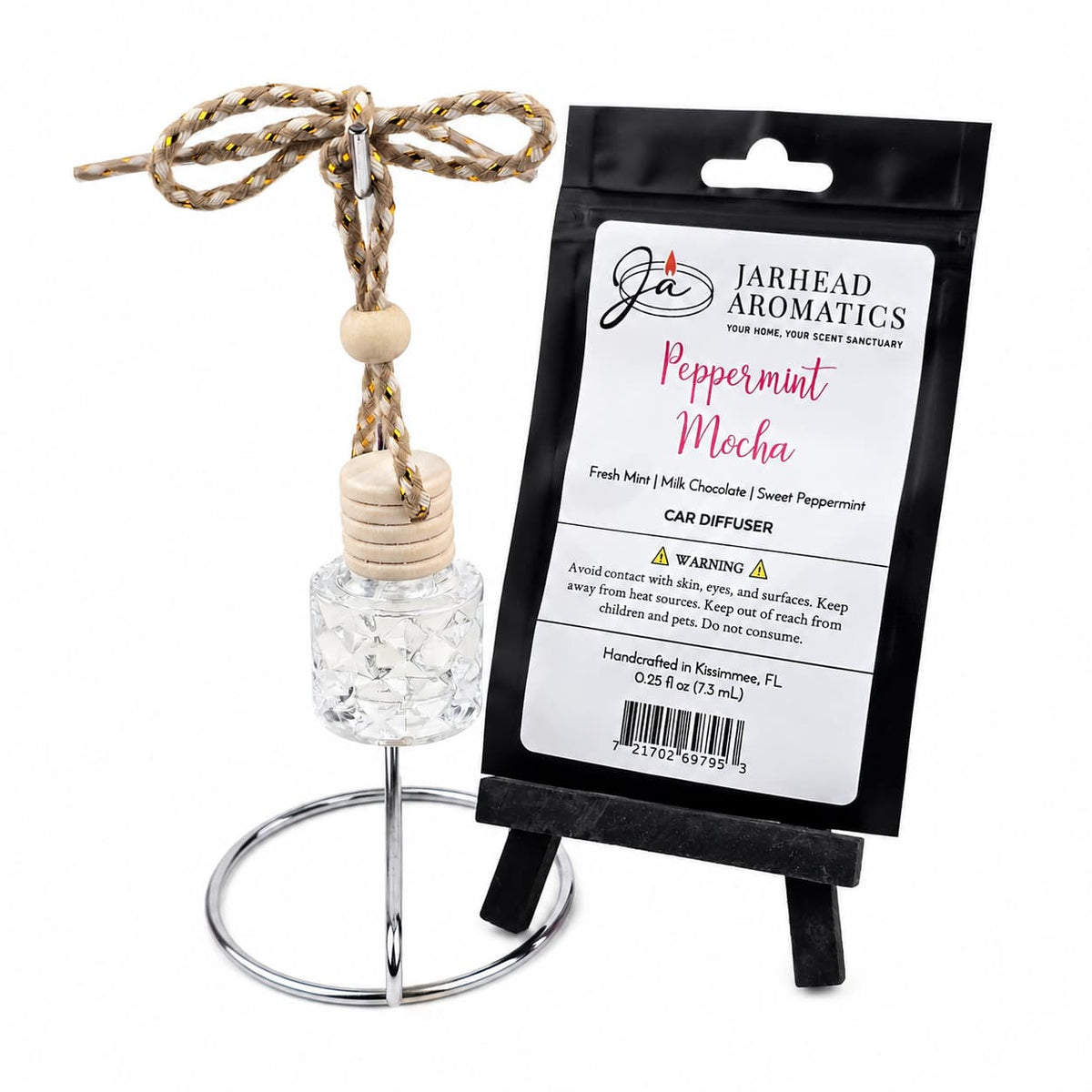 A small Jarhead Aromatics Peppermint Mocha Car Diffuser | Chocolate Mint bottle with a wooden cap and rope hanger stands on a metal ring display next to its black product packaging.