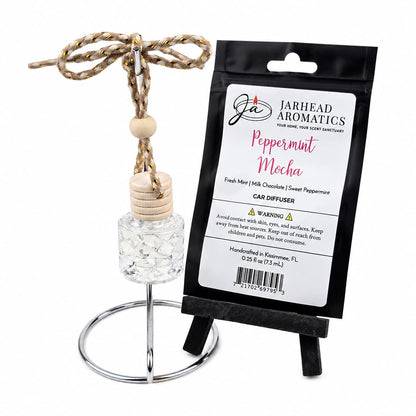 A small Jarhead Aromatics Peppermint Mocha Car Diffuser | Chocolate Mint bottle with a wooden cap and rope hanger stands on a metal ring display next to its black product packaging.