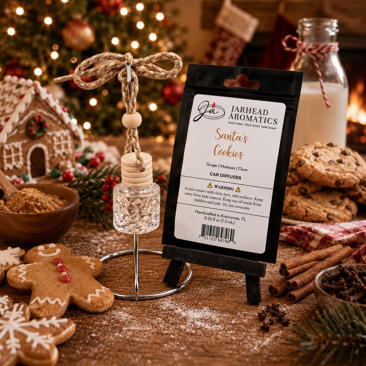 A Jarhead Aromatics Santa’s Cookies Car Diffuser featuring a glass bottle and wooden cap, displayed next to its packaging on a small easel, surrounded by gingerbread cookies and holiday decor.