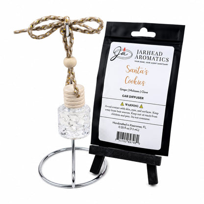 A small Santa’s Cookies Car Diffuser hanging from a metal stand next to its product packaging.