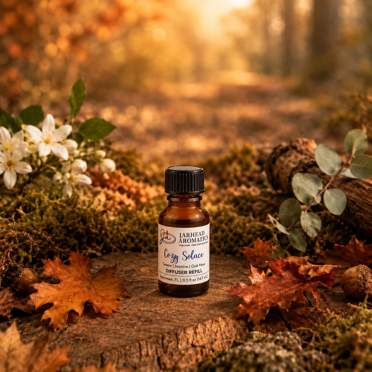 A small bottle of Jarhead Aromatics Cozy Solace Cold Air Diffuser Refill—featuring fresh greens, jasmine, and oak moss—rests on a bed of moss surrounded by autumn leaves, flowers, and a fallen log in a sun-dappled forest setting, evoking the essence of an autumn woodland for your home fragrance needs.