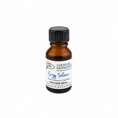 A small brown glass bottle labeled Jarhead Aromatics Cozy Solace Cold Air Diffuser Refill, featuring a home fragrance blend of fresh greens, jasmine, and oak moss—perfect as a home fragrance oil—displayed on a white background.