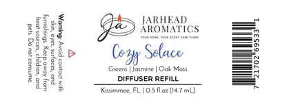 Jarhead Aromatics Cozy Solace Cold Air Diffuser Refill features a clean white label with black, blue, and gold text. The 0.5 fl oz home fragrance oil is crafted in Kissimmee, FL, and displays warnings and scent notes of fresh greens, jasmine, and oak moss for an autumn forest-inspired aroma.