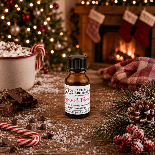 A brown glass bottle of Jarhead Aromatics Peppermint Mocha Cold Air Diffuser Refill sits on a wooden surface surrounded by chocolate, peppermint candies, and a mug of hot cocoa, with a Christmas tree and fireplace in the background.