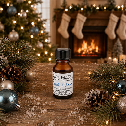 A small amber bottle of Tinsel & Timber Cold Air Diffuser Refill sits on a wooden surface, surrounded by pine branches and Christmas ornaments, with a festive fireplace in the background to evoke a winter forest scent.