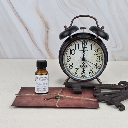 A vintage-style alarm clock, a brown envelope tied with string, two large antique keys, and a Jarhead Aromatics Maritime Escape - Cold Air Diffuser Refill are arranged on a light surface against a marble-patterned background.