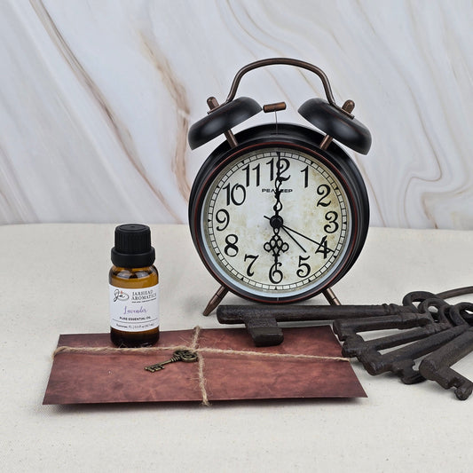A black vintage alarm clock, Jarhead Aromatics Lavender - Pure Essential Oil, a tied brown envelope with a key, and three large antique keys sit on a light surface against marble—ideal for aromatherapy lovers.