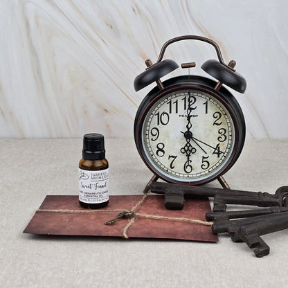 A vintage alarm clock shows 10:12 beside Jarhead Aromatics’ Sweet Fennel Pure Therapeutic-Grade Essential Oil, a twine-tied brown envelope, and two antique keys on beige with a marble-patterned background.