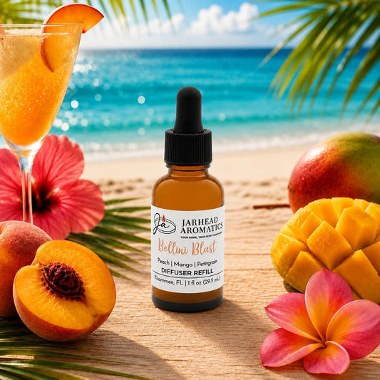 A dropper bottle labeled Bellini Blast Car Diffuser Refill from Jarhead Aromatics rests on a tropical beach, surrounded by peaches, mangoes, tangerines, a fruity drink, and tropical flowers—evoking the refreshing scent of peach, mango, and tangerine—with the ocean and palm leaves in the background.