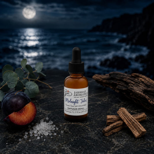 A dropper bottle labeled Midnight Tides rests on a dark stone surrounded by plum, salt, wood, leaves, and a moonlit ocean—an evocative scene that captures the essence of Jarhead Aromatics’ Midnight Tides Car Diffuser Refill in Sea Salt, Sandalwood & Dark Musk.