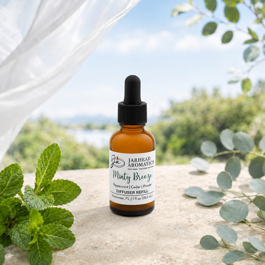 A brown glass dropper bottle labeled Minty Breeze Car Diffuser Refill by Jarhead Aromatics rests on a stone surface outdoors, encircled by green leaves with a softly lit background of trees and sky. Ideal as a car diffuser refill, this peppermint, eucalyptus, and cedarwood fragrance brings the crisp freshness of the outdoors into your drive.