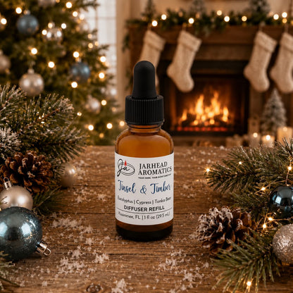 A brown glass dropper bottle of Tinsel & Timber Car Diffuser Refill sits on a wooden surface surrounded by holiday decorations, pine branches, and ornaments in front of a fireplace.