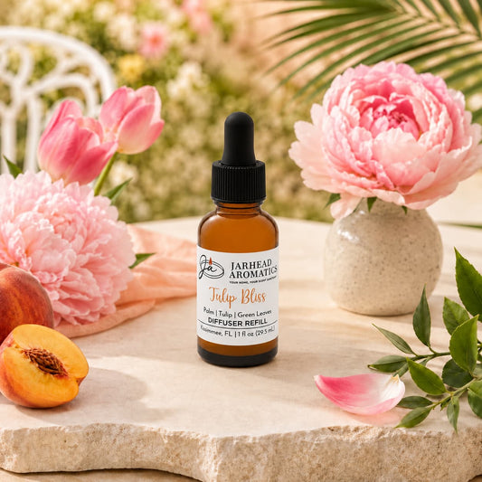 A bottle of Jarhead Aromatics Tulip Bliss Car Diffuser Refill (Tulip, Peony & Sweet Peach) rests on a stone surface, surrounded by pink flowers, green leaves, and a peach, capturing the essence of a garden-inspired air freshener with a sunlit garden in the background.