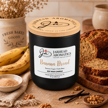A Banana Bread Soy Wax Candle | Banana, Sugar & Tonka Bean by Jarhead Aromatics in a glass jar with a wooden lid, surrounded by slices of banana bread, whole bananas, brown sugar, and vanilla beans.