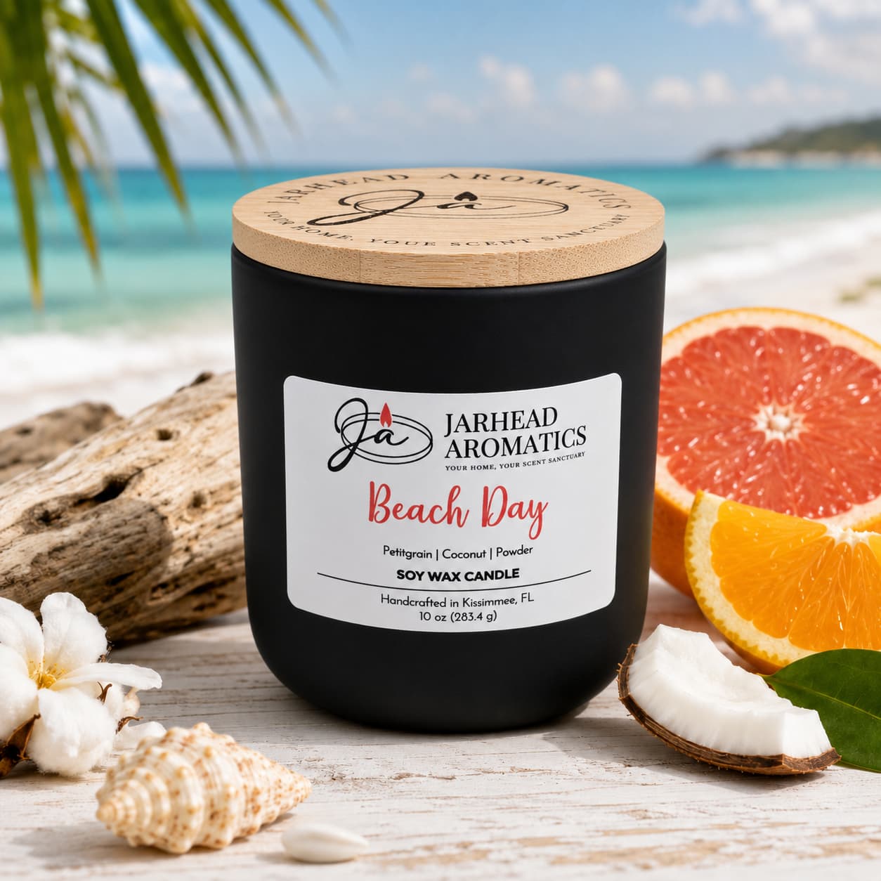 A black Jarhead Aromatics Beach Day Soy Wax Candle | Coconut, Citrus & Coastal Breeze Candle rests on the beach surrounded by palm leaves, seashells, a slice of grapefruit, coconut, and ocean waves in the background, infusing the air with its coastal fragrance and a long-lasting scent reminiscent of sun-drenched shores.