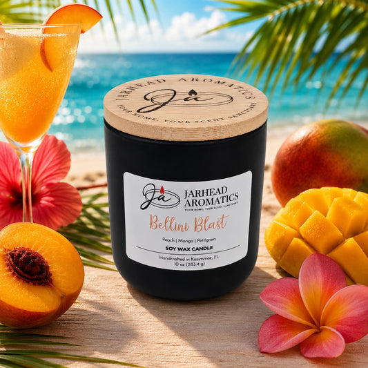 A Jarhead Aromatics Bellini Blast Soy Wax Candle with peach, mango, and tangerine scents rests on sand among tropical fruits and flowers, with ocean and palm trees in the background, capturing its vibrant tropical aroma.