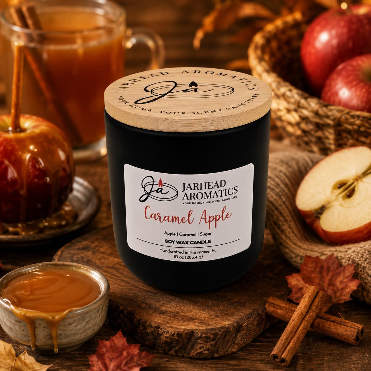 A Jarhead Aromatics Caramel Apple Soy Wax Candle rests on a wooden table surrounded by caramel, cinnamon sticks, apples, and a caramel apple, filling the space with its warm apple cider, caramel, and sugar fragrance for a cozy autumn ambiance.
