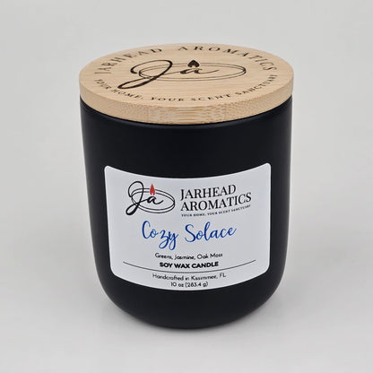 A black soy wax candle jar with a wooden lid from Jarhead Aromatics, the Cozy Solace Soy Wax Candle showcases a blend of fresh greens, jasmine, oak moss, and musk. Hand-poured in Kissimmee, FL, this autumn-inspired candle captures an inviting seasonal fragrance.
