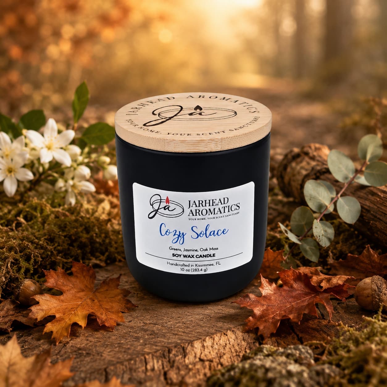 A hand-poured Cozy Solace Soy Wax Candle from Jarhead Aromatics rests atop autumn leaves and moss, surrounded by flowers and foliage, with a blurred forest backdrop—capturing the essence of fresh greens, jasmine, oak moss, and musk in a warm fall fragrance.