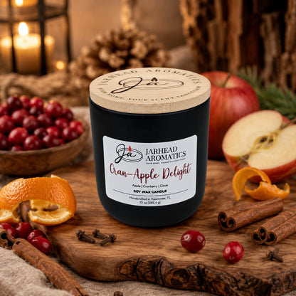 A Jarhead Aromatics Cran-Apple Delight Soy Wax Candle, featuring notes of cranberry, apple, and cinnamon, sits on a wooden tray surrounded by cranberries, apple slices, orange peel, cinnamon sticks, and pine cones. This beautifully scented candle fills the air with a warm autumn fragrance, while a softly glowing candle and seasonal décor create a blurred backdrop.
