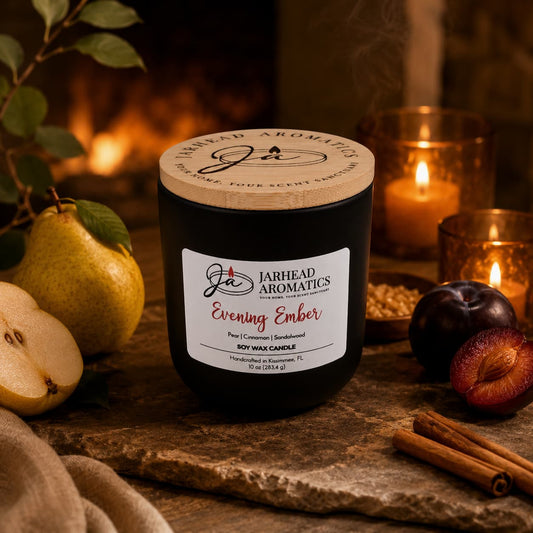 A Jarhead Aromatics Evening Ember Soy Wax Candle | Plum, Sandalwood & Smoke Candle rests on a rustic table surrounded by pears, plums, cinnamon sticks, and a glowing fireplace in the background. Made from premium soy wax, this candle fills the space with plum, sandalwood, and smoke notes for a cozy autumn ambiance that radiates warmth and relaxation.