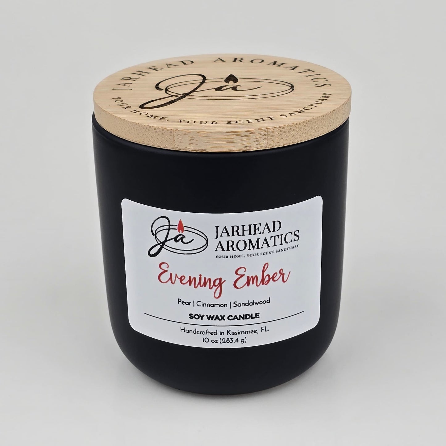 A black candle jar with a wooden lid labeled Jarhead Aromatics Evening Ember Soy Wax Candle, featuring premium soy wax infused with plum, sandalwood, and smoke scents. The 10 oz jar is handcrafted in Kissimmee, FL.