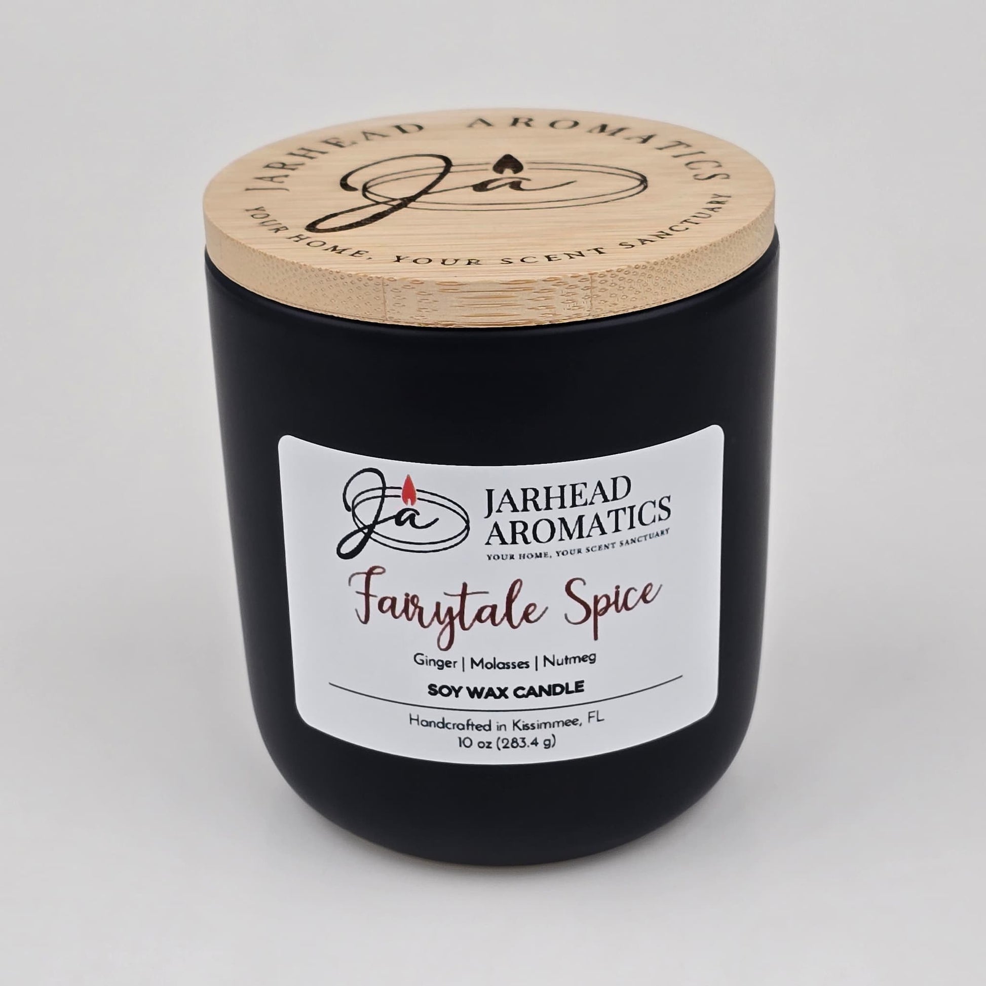 A black candle jar with a wooden lid from Jarhead Aromatics, labeled Fairytale Spice Soy Wax Candle | Gingerbread, Cinnamon & Vanilla Candle. This handcrafted holiday candle is made in Kissimmee, FL with soy wax and features festive scents of gingerbread, cinnamon, and vanilla—perfect for bringing warmth and cheer to your home.
