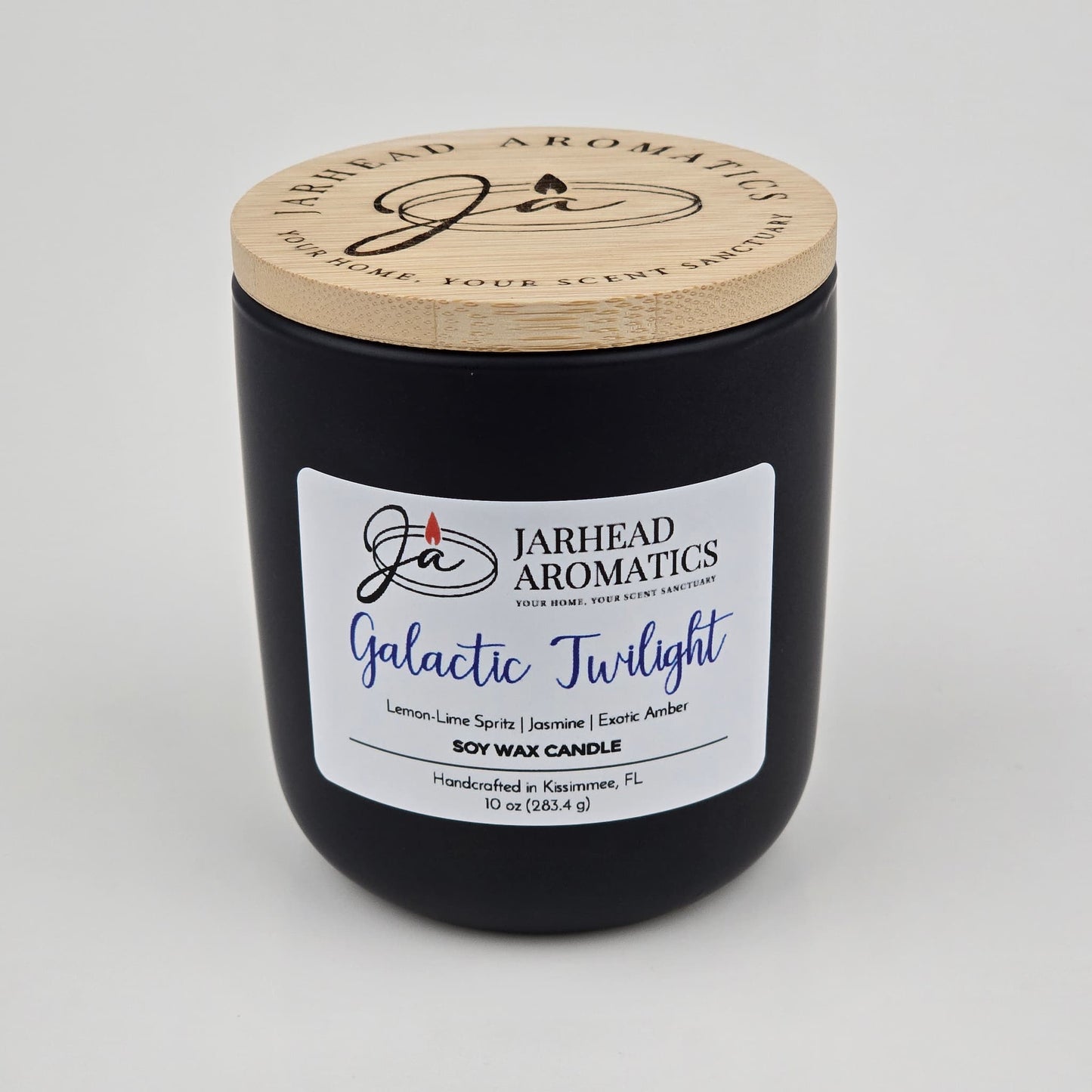 A handcrafted black soy wax candle jar from Jarhead Aromatics, labeled Galactic Twilight Soy Wax Candle, features bergamot, jasmine, and amber scents. Made in Kissimmee, FL with a wooden lid.