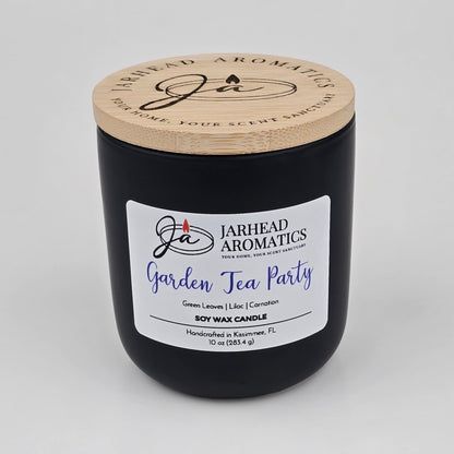 A black Jarhead Aromatics hand-poured soy wax candle, labeled Garden Tea Party, featuring notes of rose, jasmine, and green floral accords. This candle is handcrafted in Kissimmee, FL and comes with a wooden lid.