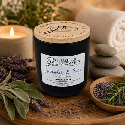 The Lavender & Sage Soy Wax Candle by Jarhead Aromatics, scented with lavender, sage & sandalwood, rests on wood amid fresh herbs and stones—a spa-like scene to enjoy its relaxing aroma.