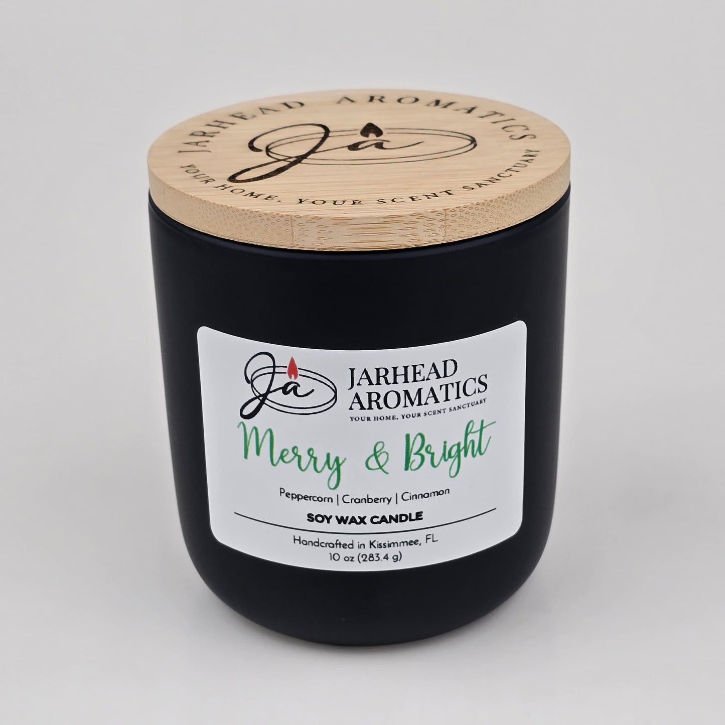 A black candle jar with a wooden lid labeled Jarhead Aromatics Merry & Bright. The Merry & Bright Soy Wax Candle by Jarhead Aromatics brings a festive holiday ambiance with notes of citrus cranberry, warm spice, and fir—making it the perfect handcrafted holiday candle from Kissimmee, FL.