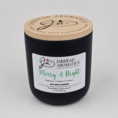A black candle jar with a wooden lid labeled Jarhead Aromatics Merry & Bright. The Merry & Bright Soy Wax Candle by Jarhead Aromatics brings a festive holiday ambiance with notes of citrus cranberry, warm spice, and fir—making it the perfect handcrafted holiday candle from Kissimmee, FL.