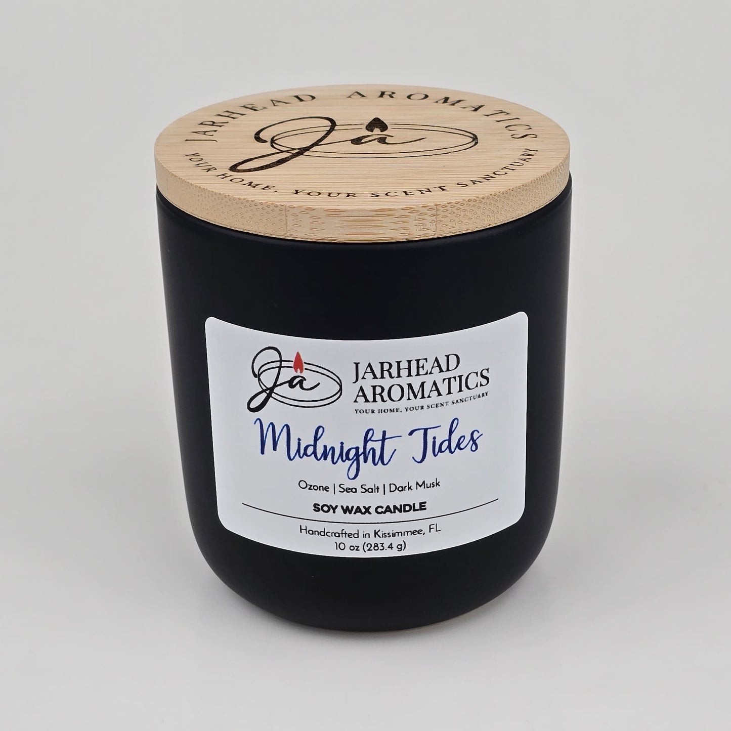 Experience the refreshing allure of ocean air with the Midnight Tides Soy Wax Candle from Jarhead Aromatics. Handcrafted in Kissimmee, FL, this black soy wax candle features a wooden lid and is labeled "Jarhead Aromatics Midnight Tides." With scent notes of ozone, sea salt, dark musk, and sandalwood, it captures the invigorating essence of coastal breezes.