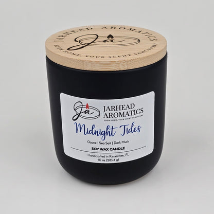 Experience the refreshing allure of ocean air with the Midnight Tides Soy Wax Candle from Jarhead Aromatics. Handcrafted in Kissimmee, FL, this black soy wax candle features a wooden lid and is labeled "Jarhead Aromatics Midnight Tides." With scent notes of ozone, sea salt, dark musk, and sandalwood, it captures the invigorating essence of coastal breezes.