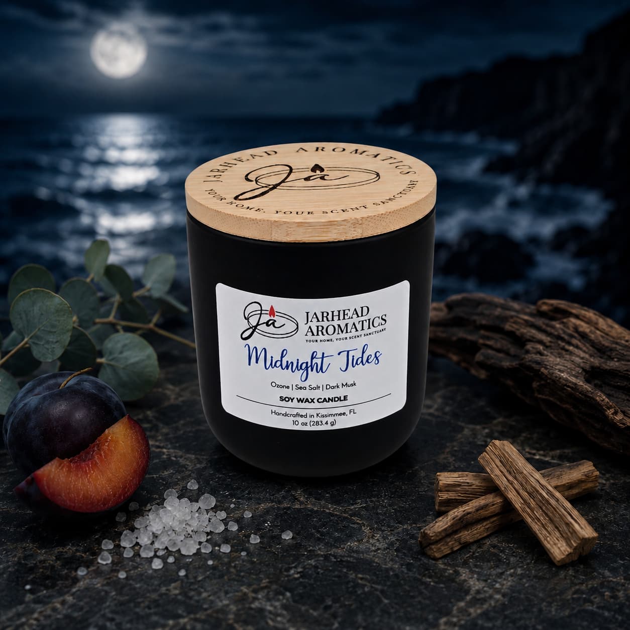 A hand-poured Midnight Tides Soy Wax Candle | Sea Salt, Dark Musk & Sandalwood by Jarhead Aromatics rests on a rocky surface with driftwood, salt, plum, and eucalyptus nearby, set against a moonlit ocean and rugged coastline—capturing the essence of a true coastal fragrance candle.