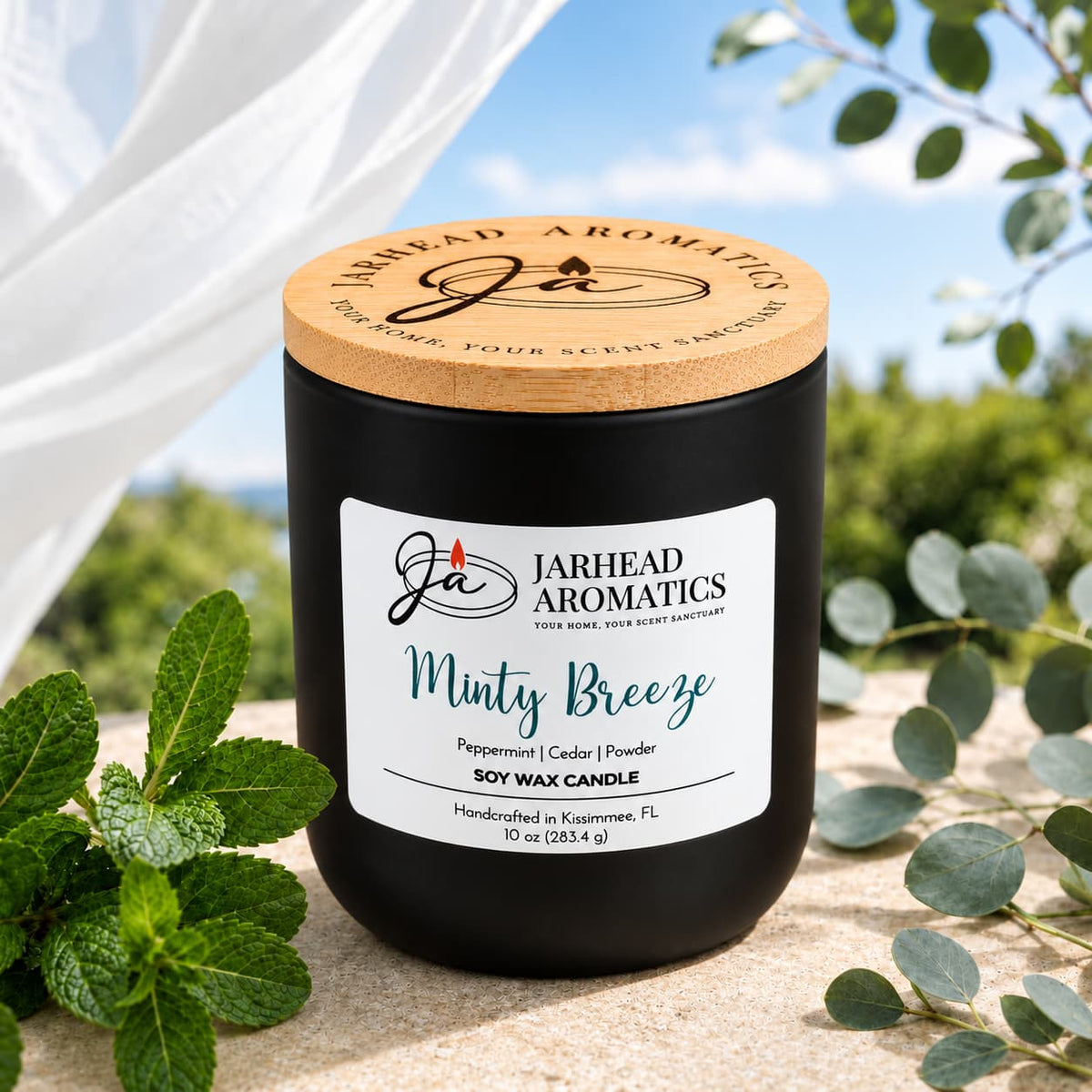A black Minty Breeze Soy Wax Candle with a wooden lid sits on a stone surface next to fresh mint sprigs.