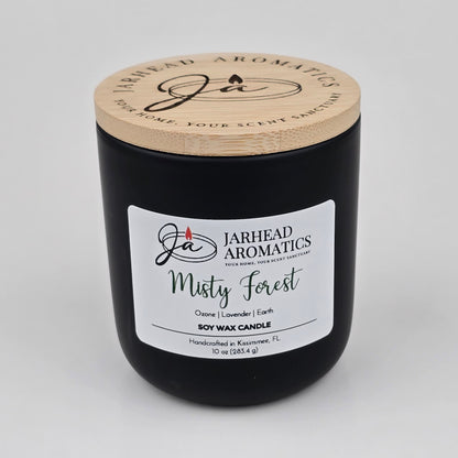 A 10 oz black soy wax candle in a jar with a wooden lid labeled “Jarhead Aromatics Misty Forest,” handcrafted in Kissimmee, FL. The Misty Forest Soy Wax Candle by Jarhead Aromatics features earthy moss, lavender, and juniper scents for a soothing, nature-inspired fragrance.