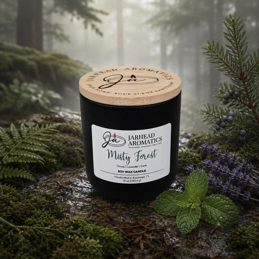 A black Jarhead Aromatics Misty Forest Soy Wax Candle rests on a bed of moss, surrounded by lavender, juniper, and pine branches, with a misty forest in the background. This candle combines natural soy wax with earthy moss, lavender, and juniper scents to bring the tranquil aroma of the woods into your space.