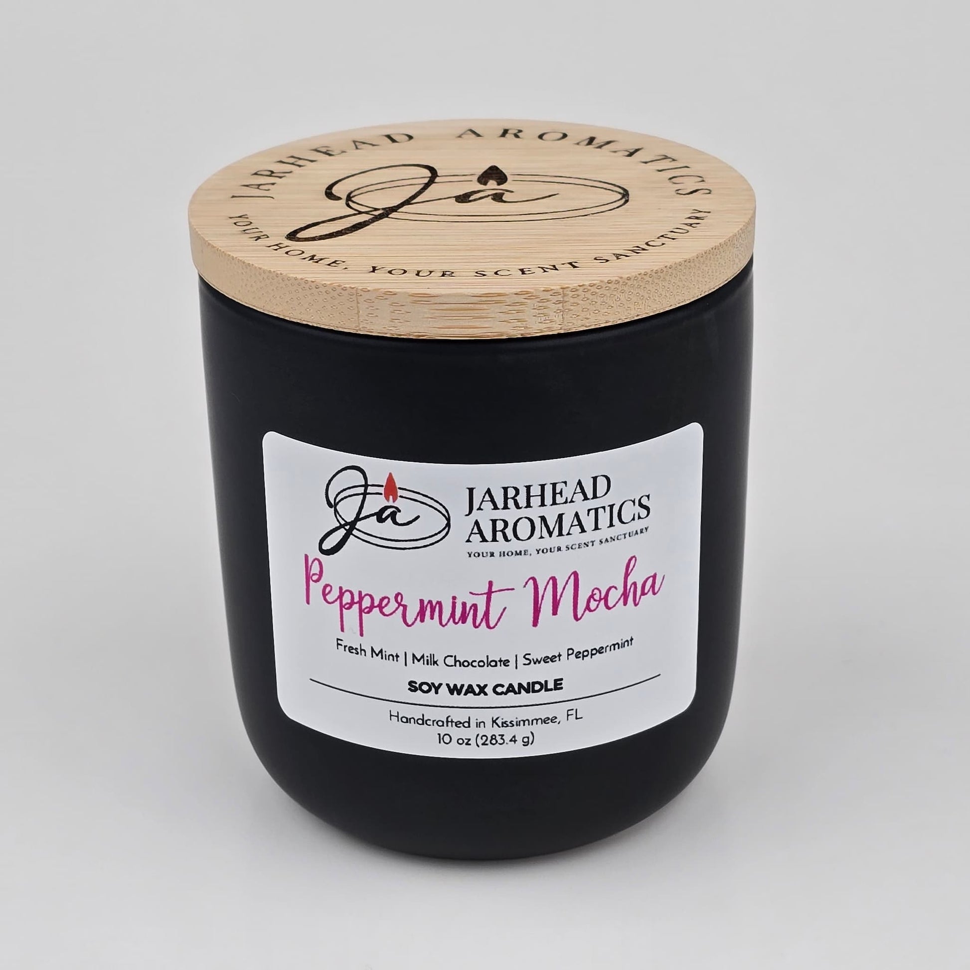 This Peppermint Mocha Soy Wax Candle by Jarhead Aromatics comes in a sleek black jar with a wooden lid. The white label describes scent notes of fresh mint, milk chocolate, and sweet peppermint, creating the perfect holiday ambiance. Featuring the comforting aroma of chocolate mint and vanilla, this 10 oz candle is an ideal choice for anyone who enjoys festive fragrances during the holiday season.