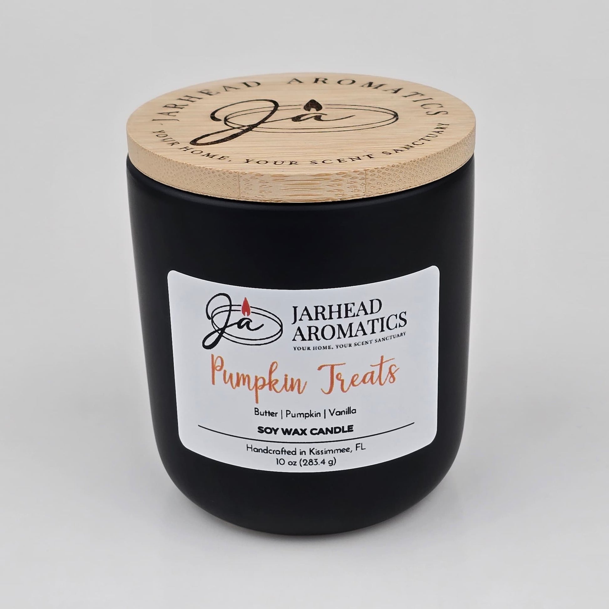 A black jar candle with a wooden lid from Jarhead Aromatics, labeled “Pumpkin Treats Soy Wax Candle,” features cozy autumn notes of pumpkin caramel, maple pecan, and vanilla. Handcrafted in Kissimmee, FL and made from soy wax, this Fall Candle is perfect for adding a warm seasonal touch to your space.