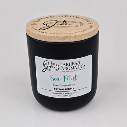 A black candle jar with a wooden lid from Jarhead Aromatics, labeled Sea Mist Soy Wax Candle | Clean Coastal Linen & Sea Salt Candle, featuring an invigorating aquatic floral fragrance of linen, eucalyptus, and moss. This coastal candle is handcrafted in Kissimmee, FL and contains 10 oz (283.4 g).