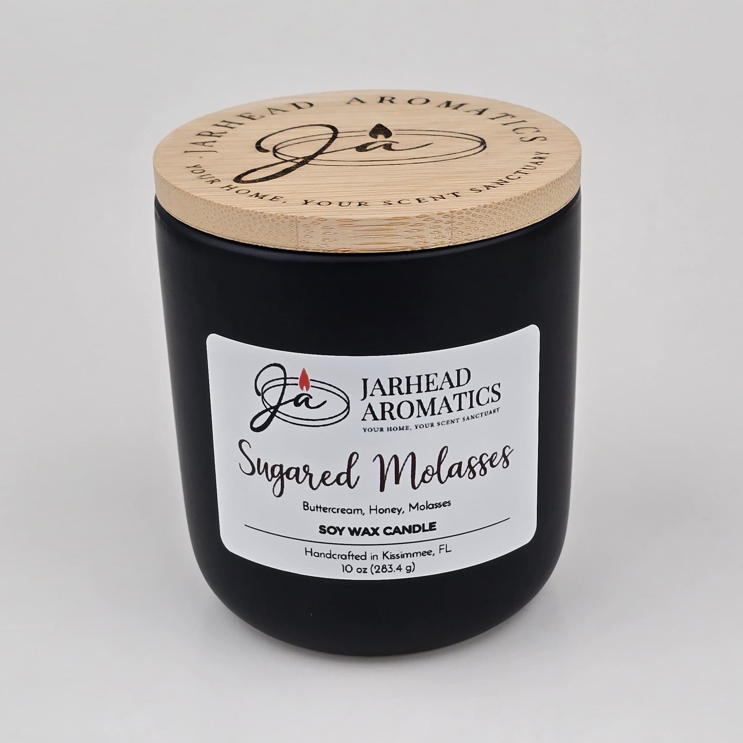 A black candle jar with a wooden lid labeled Jarhead Aromatics Sugared Molasses Soy Wax Candle | Brown Sugar, Honey, Cinnamon & Molasses Fall Candle, a hand-poured soy candle featuring a gourmand blend of brown sugar, honey, cinnamon, and molasses. This handcrafted candle is made in Kissimmee, FL.