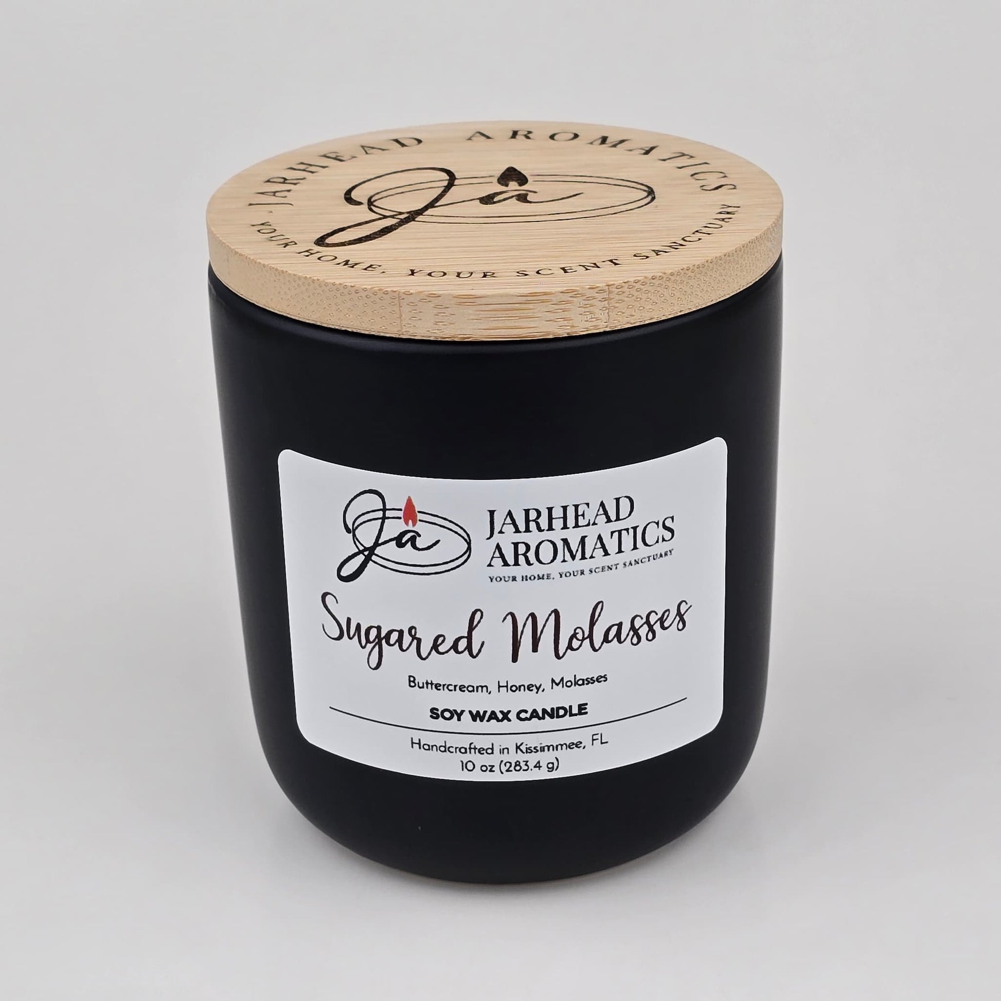 A black candle jar with a wooden lid labeled Jarhead Aromatics Sugared Molasses Soy Wax Candle | Brown Sugar, Honey, Cinnamon & Molasses Fall Candle, a hand-poured soy candle featuring a gourmand blend of brown sugar, honey, cinnamon, and molasses. This handcrafted candle is made in Kissimmee, FL.