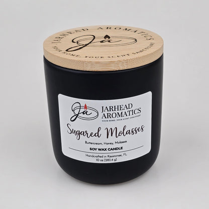 A black candle jar with a wooden lid labeled Jarhead Aromatics Sugared Molasses Soy Wax Candle | Brown Sugar, Honey, Cinnamon & Molasses Fall Candle, a hand-poured soy candle featuring a gourmand blend of brown sugar, honey, cinnamon, and molasses. This handcrafted candle is made in Kissimmee, FL.