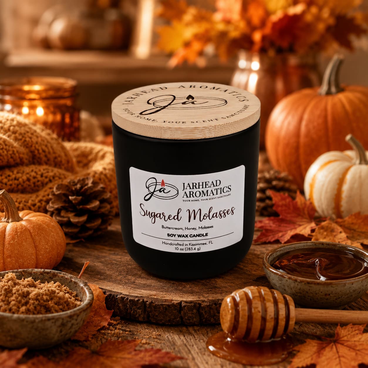 A black Jarhead Aromatics Sugared Molasses Soy Wax Candle, labeled “Sugared Molasses,” sits on a rustic wooden table surrounded by autumn leaves, pumpkins, a bowl of brown sugar, a bowl of molasses, and a honey dipper. Hand-poured and crafted with soy wax, this candle features inviting notes of brown sugar, honey, cinnamon, and molasses—creating the perfect cozy gourmand fragrance to capture the essence of fall.