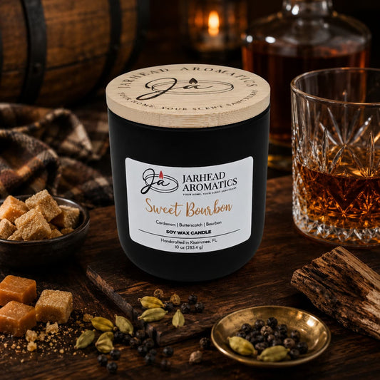 A Jarhead Aromatics Sweet Bourbon Soy Wax Candle | Warm Bourbon, Brown Sugar & Oak Candle rests on a table alongside bourbon, sugar cubes, cardamom pods, peppercorns, a plaid cloth, and a wooden barrel in the background, creating a cozy, rustic atmosphere. This hand-poured soy candle from Jarhead Aromatics fills the room with its warm notes of bourbon, brown sugar, and oak—a long-lasting scent that perfectly enhances its inviting surroundings.
